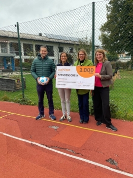 $ Personne auf dem kaputten Sportplatz bei der Scheckübergabe
